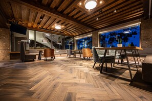 A spacious room with a wooden herringbone floor, a large window with a view of trees, and a modern interior design. - Hotel Alpina (Untertauern)