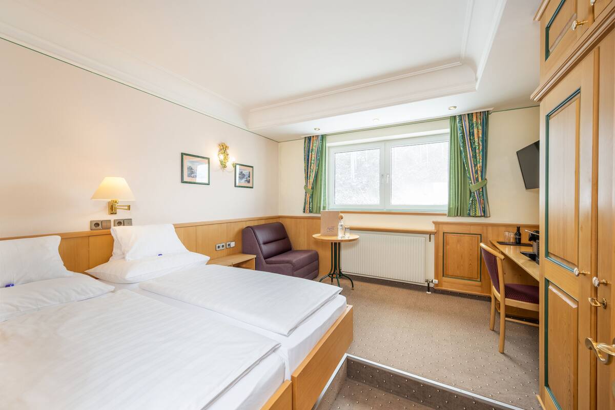 A hotel room with a bed, a desk, a chair, a small table, and a television.