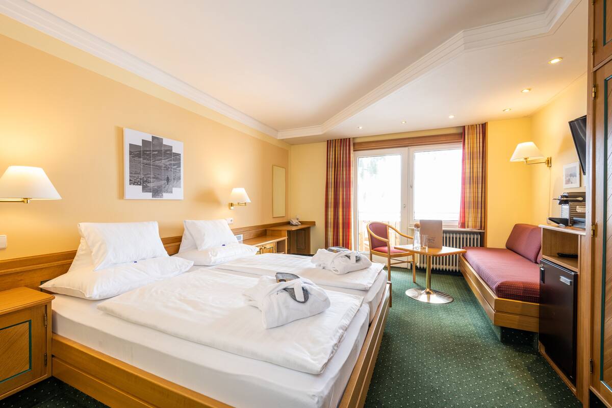 A hotel room with two beds, a desk, a chair, a TV, and a window with curtains.