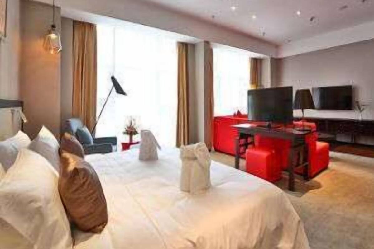 Una habitación de hotel moderna con una cama grande, un escritorio con silla, televisión y un sofá rojo.