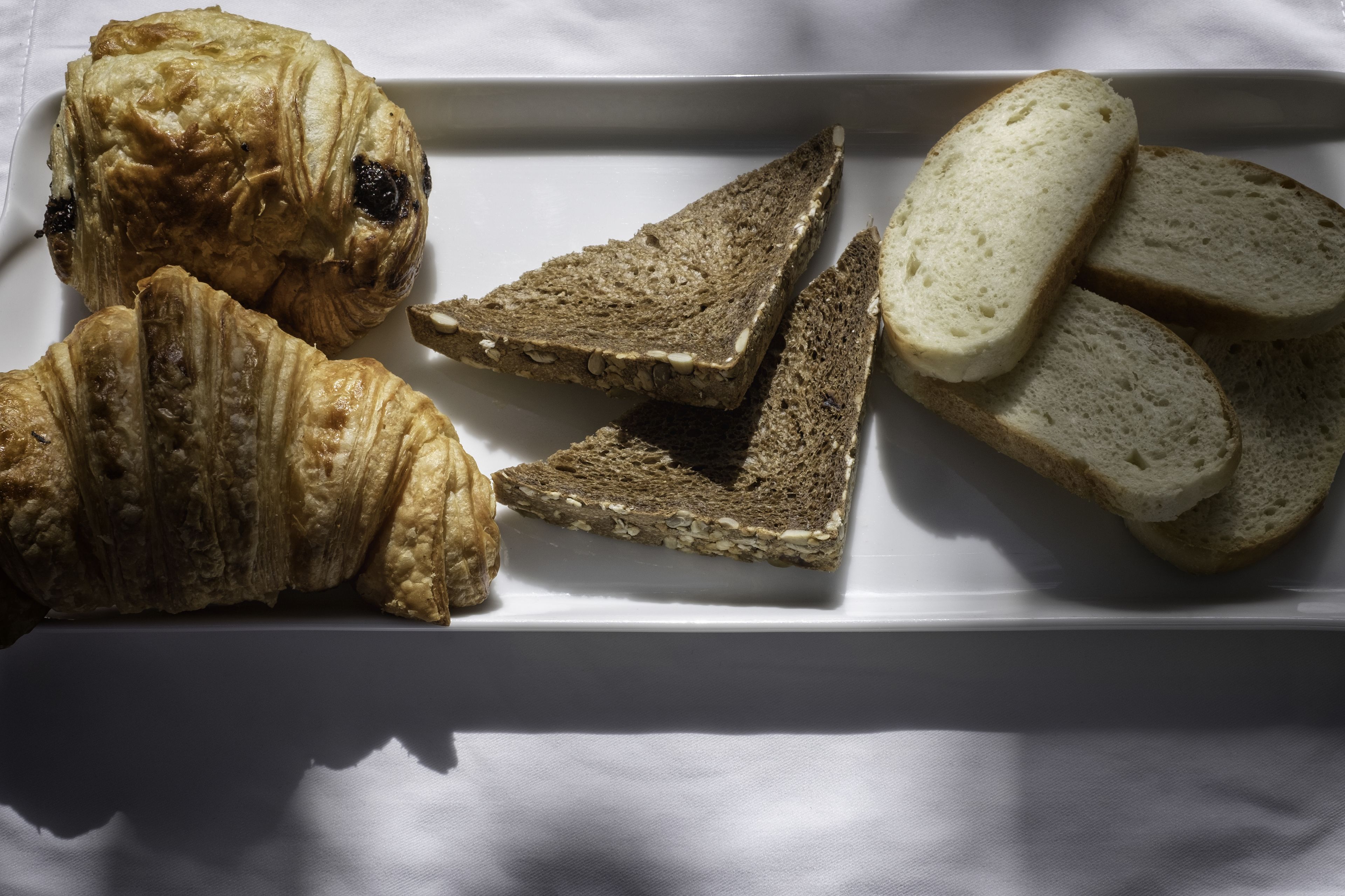 A white rectangular plate with three croissants and three slices of bread.