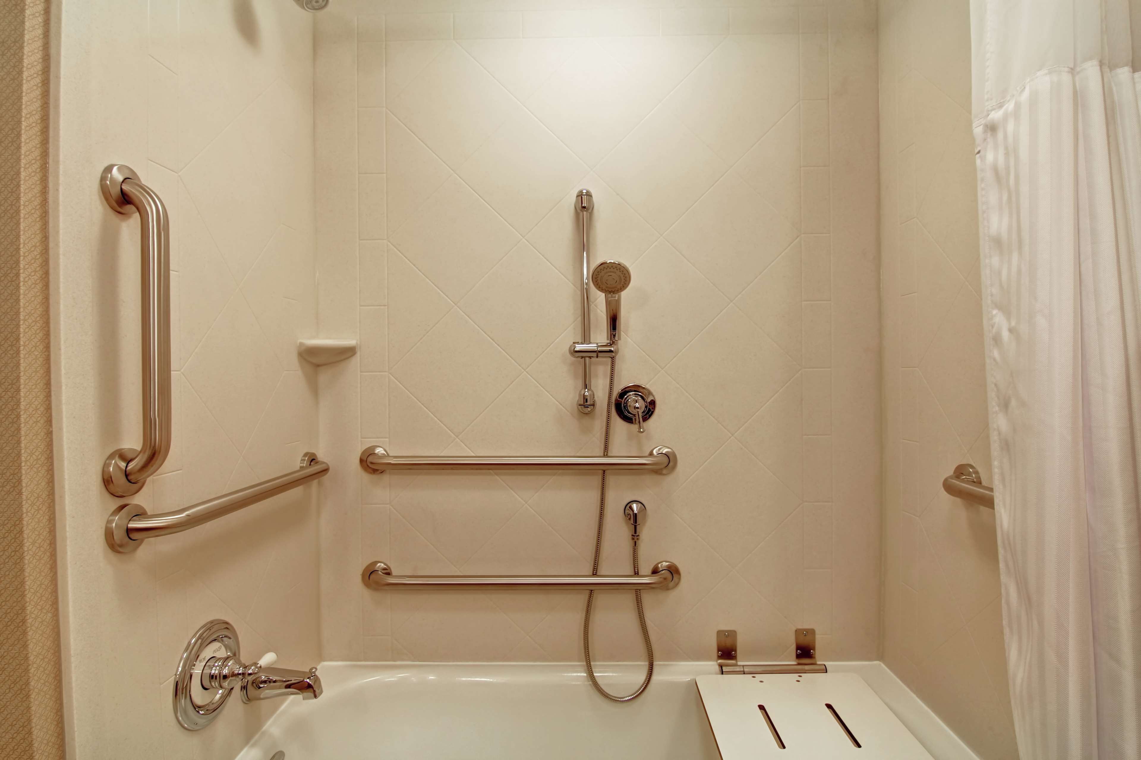 Un baño con bañera, barras de apoyo, ducha y retrete.