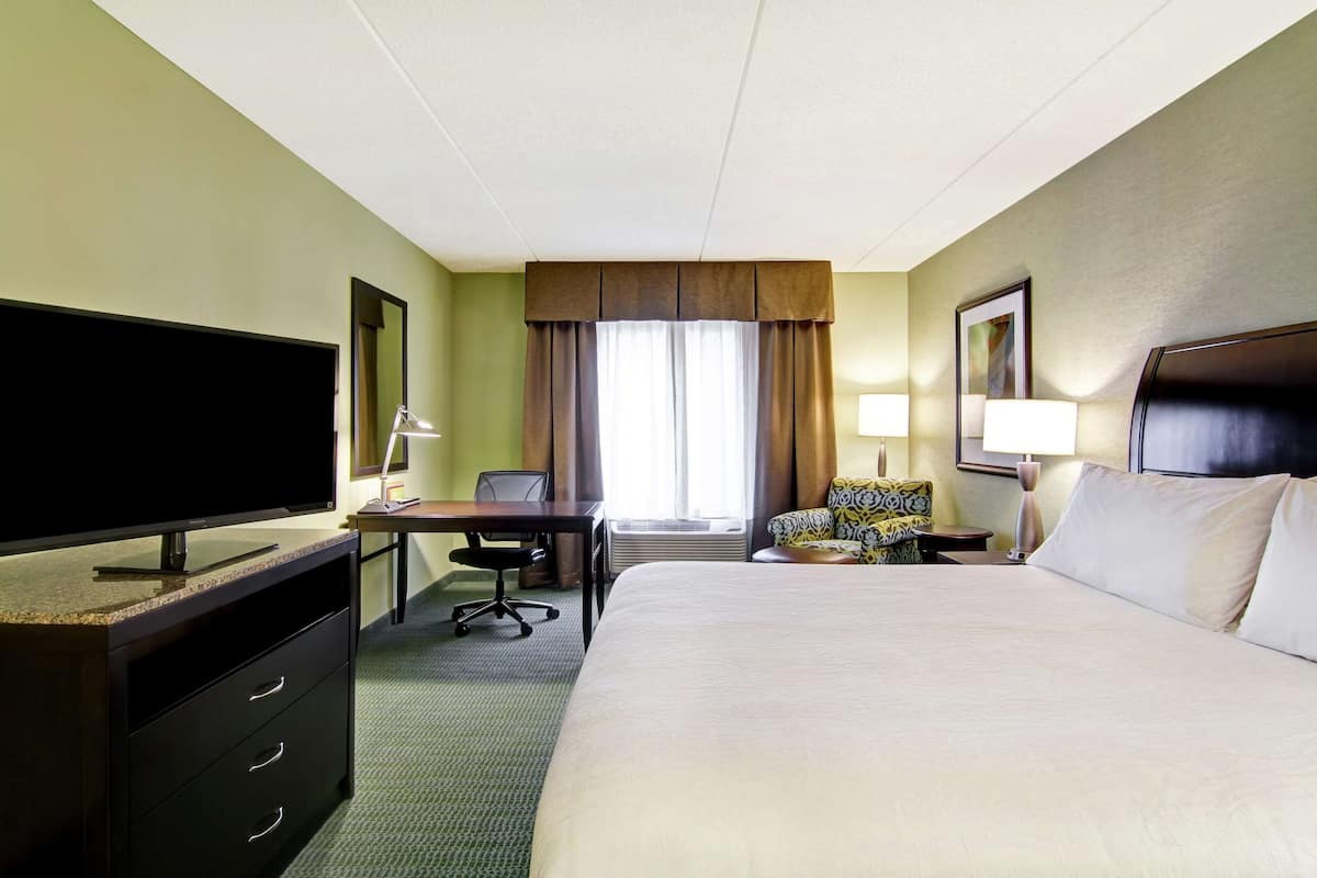 Une chambre d’hôtel avec un grand lit, un bureau avec un ordinateur, une télévision et une chaise.