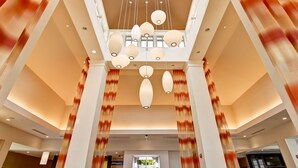 A spacious lobby with a high ceiling, multiple hanging light fixtures, and a central column structure. - Hilton Garden Inn Woodbridge (Woodbridge)