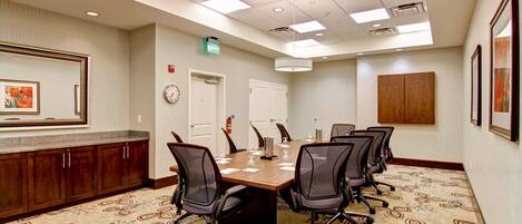 A conference room with a long table, chairs, a clock, and framed artwork on the wall.