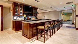 A modern kitchen with a bar area, wooden cabinets, and a large island with bar stools. - Hilton Garden Inn Woodbridge (Woodbridge)