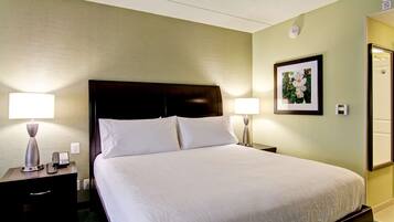 A hotel room with a large bed, two bedside tables with lamps, a framed picture on the wall, and a door to the right.