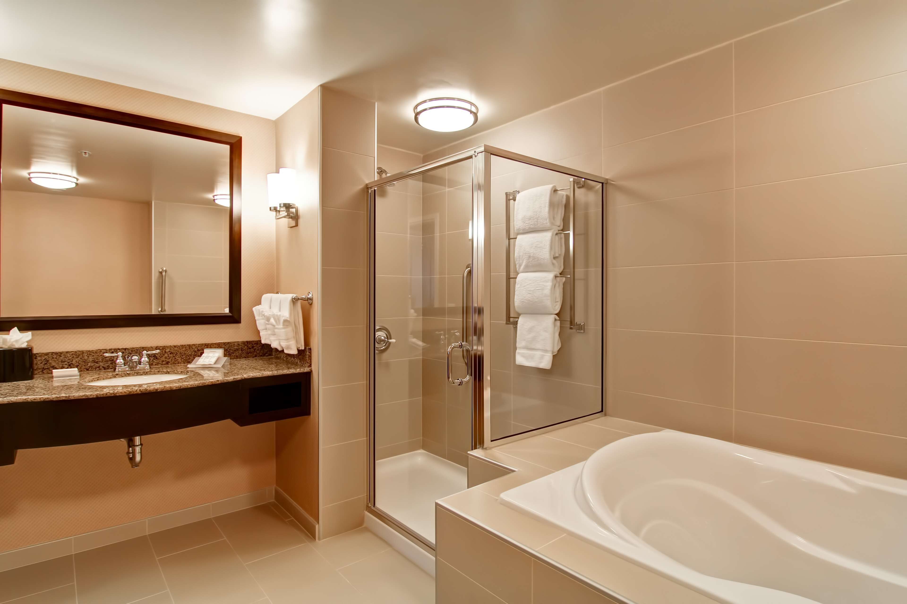Un baño moderno con ducha envuelta en vidrio, una bañera amplia y un tocador con espejo y toallero.