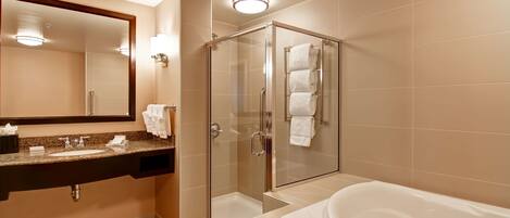 Un baño moderno con ducha envuelta en vidrio, una bañera amplia y un tocador con espejo y toallero.