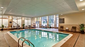 An indoor swimming pool with clear water, surrounded by seating areas and potted plants. - Hilton Garden Inn Woodbridge (Woodbridge)