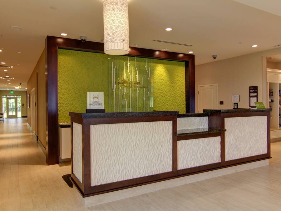 Un área de recepción con un mostrador de madera, una pared verde con textura y una lámpara instalada en el techo.