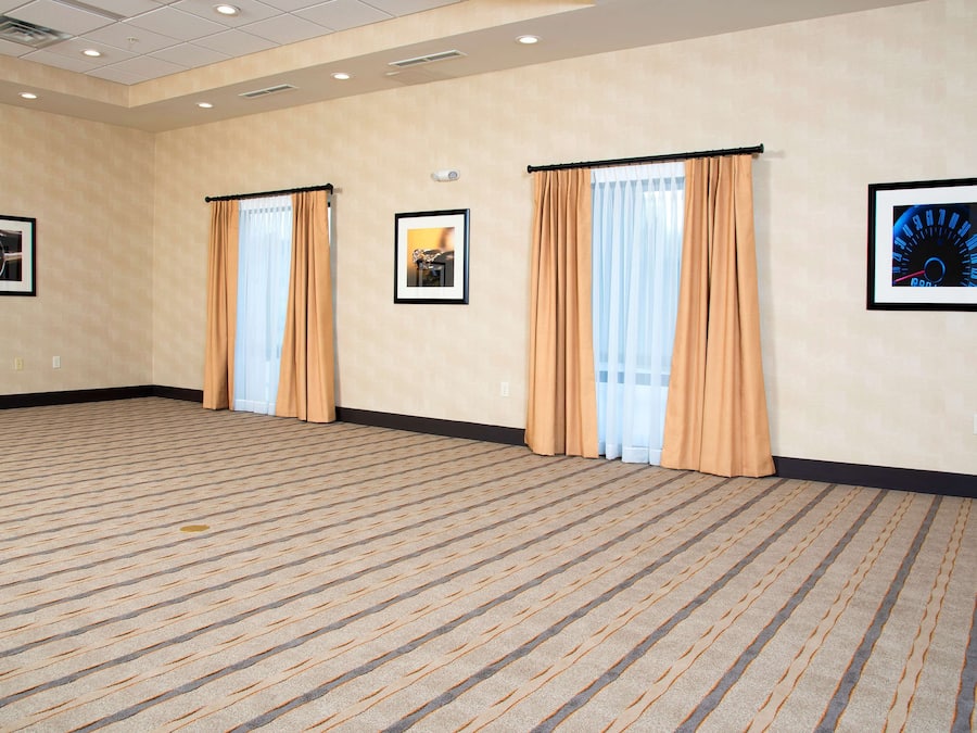 Una habitación amplia y vacía con alfombra color crema, dos puertas con cortinas color crema y tres cuadros enmarcados en las paredes.