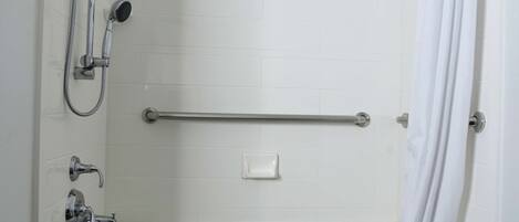 A white tiled shower area with a grab bar, a handheld showerhead, and a soap dish.
