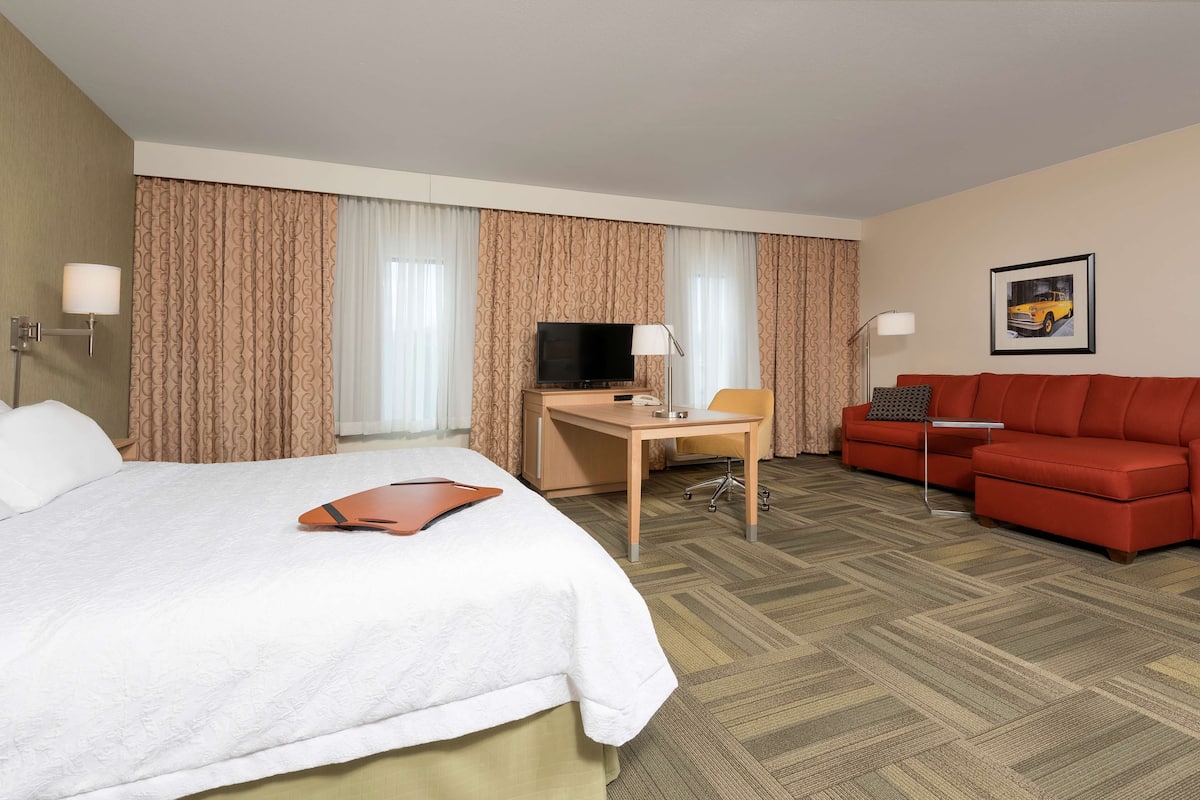 A hotel room with a bed, desk, TV, and red sofa.