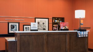 Un comptoir d’accueil orné de photos encadrées, une pancarte indiquant « Bienvenue à Kalamazoo » et une lampe.