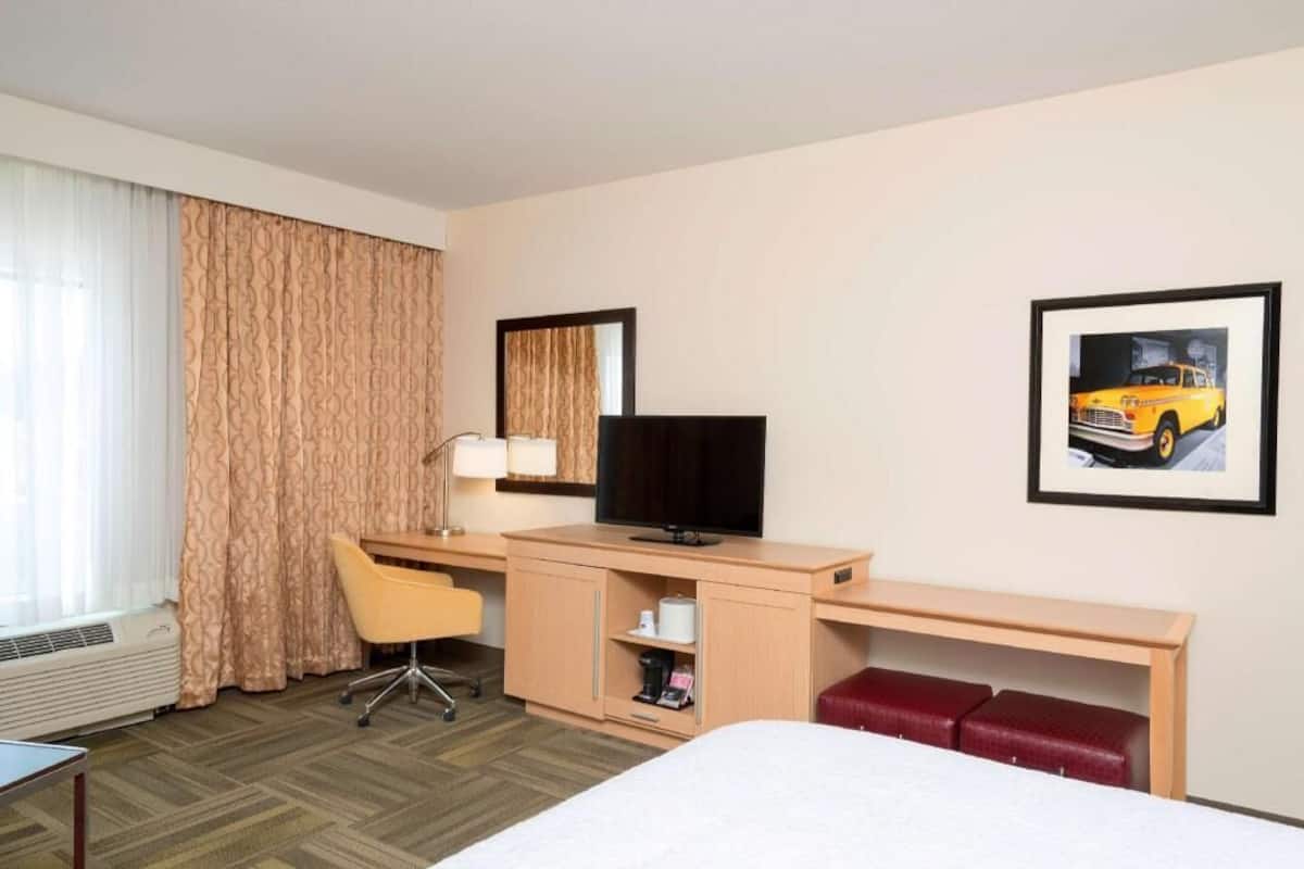 A hotel room with a bed, desk, chair, TV, and a framed picture on the wall.