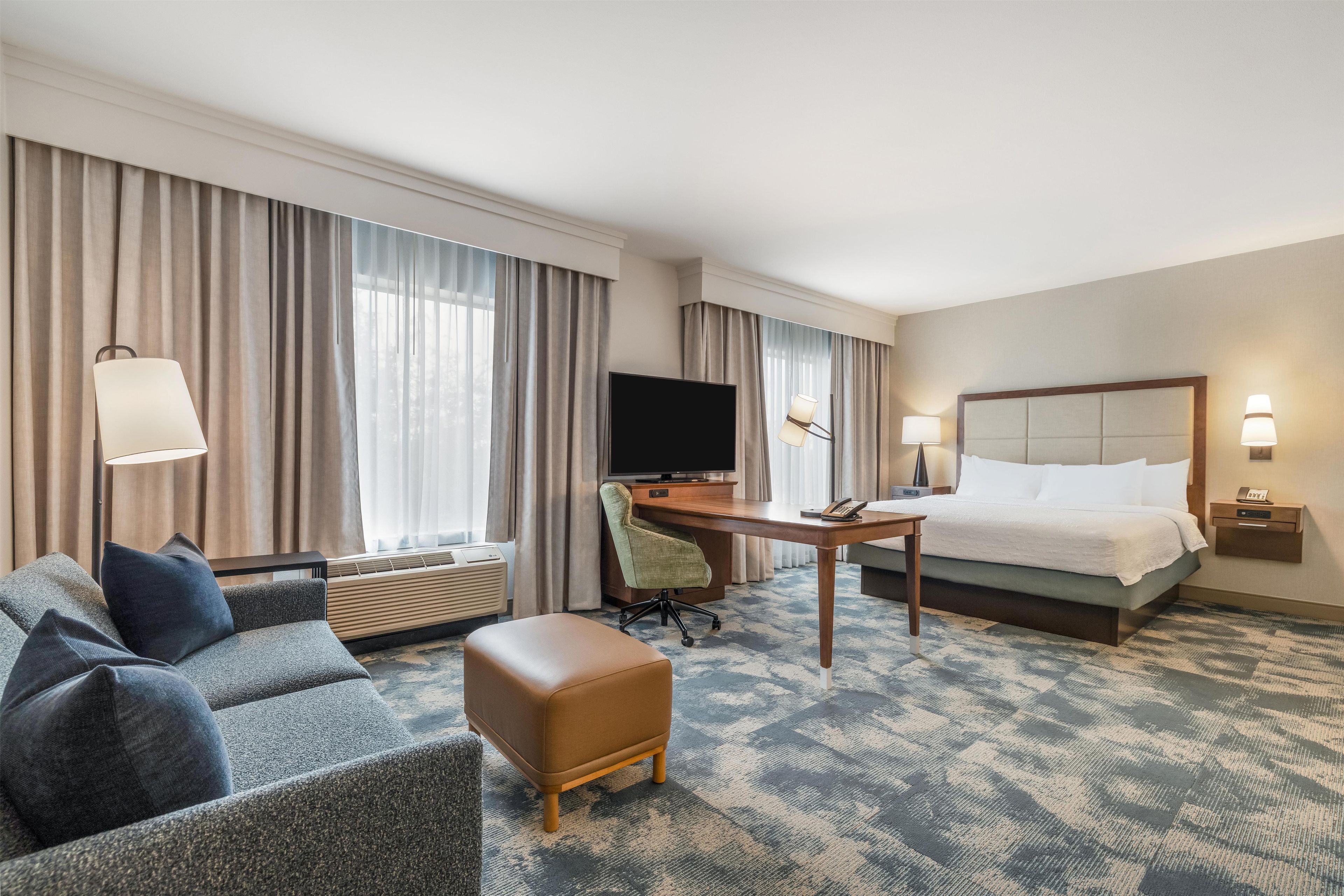 Une chambre d’hôtel équipée d’un canapé, d’un pouf, d’un bureau, d’une télévision et d’un lit.