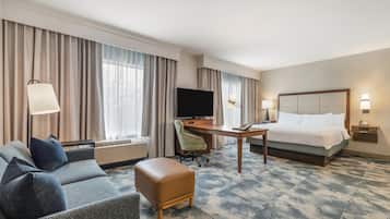 Une chambre d’hôtel équipée d’un canapé, d’un pouf, d’un bureau, d’une télévision et d’un lit.