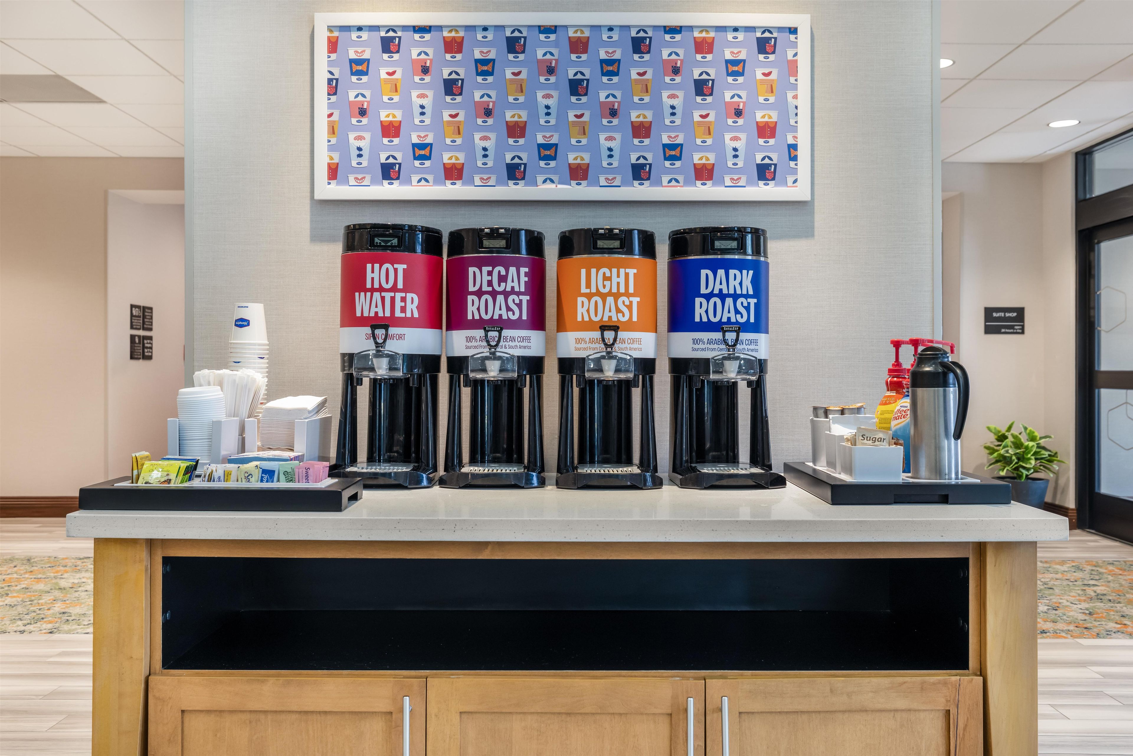 A coffee station with four coffee dispensers labeled 'Hot Water,' 'Decaf Roast,' 'Light Roast,' and 'Dark Roast.'