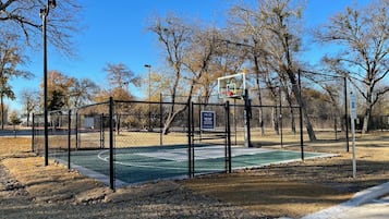 A basketball court with a chain-link fence, a basketball hoop, and a sign indicating it's a public sports court.