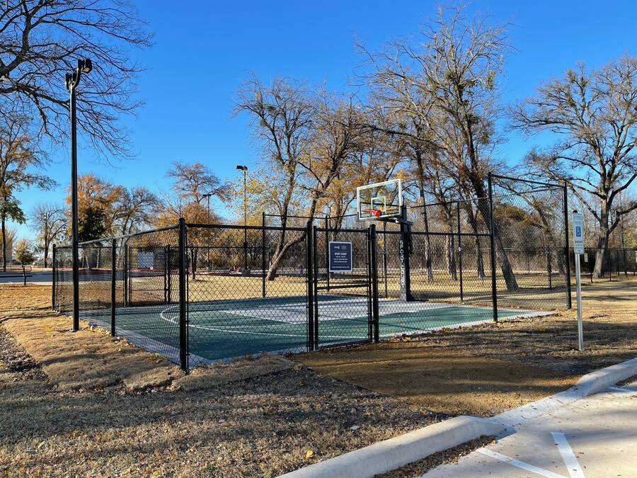 A basketball court with a chain-link fence, a basketball hoop, and a sign indicating it's a public sports court.
