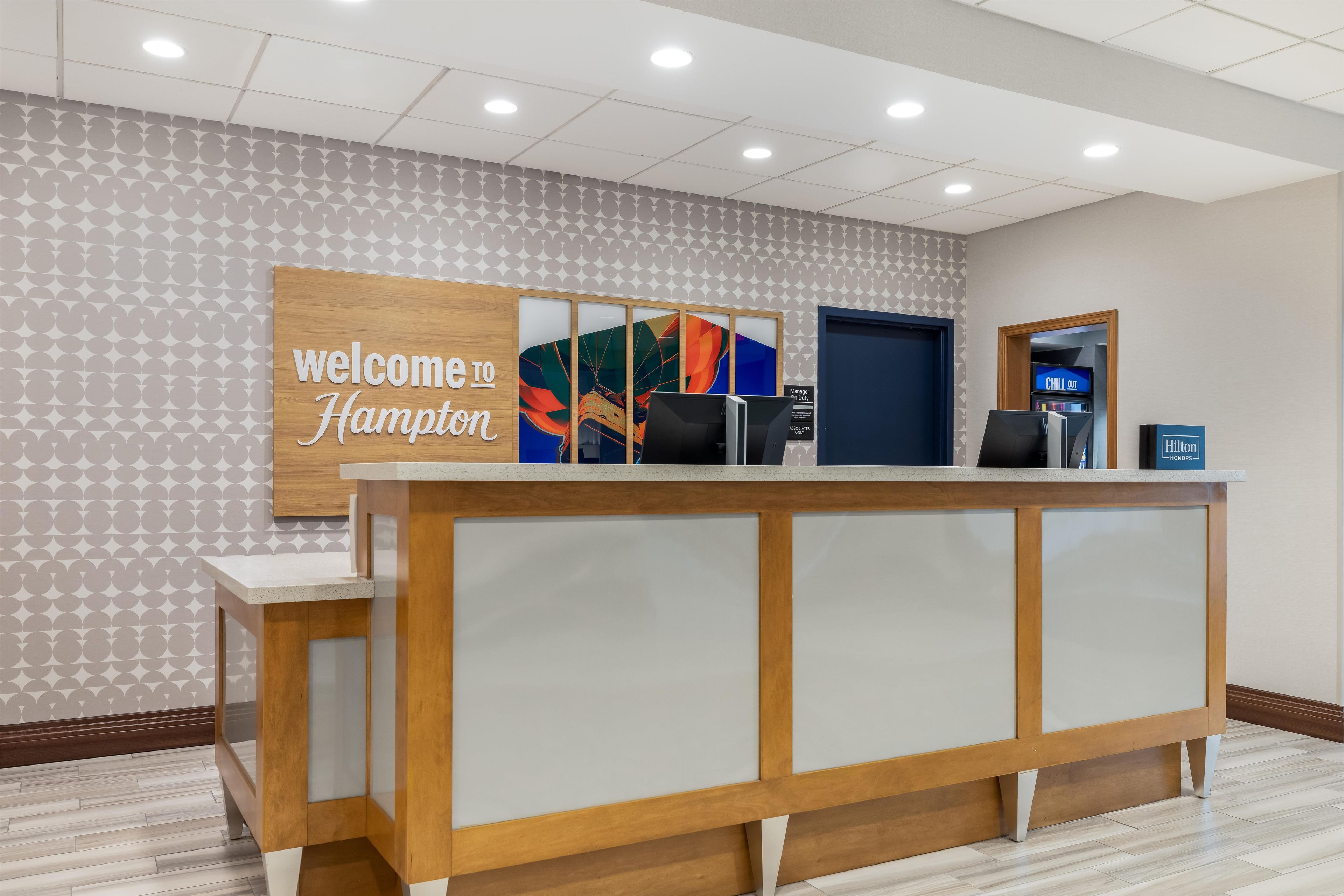 Un comptoir d’accueil avec une pancarte « Bienvenue à Hampton », un écran numérique et une pancarte « DÉTENTE ».