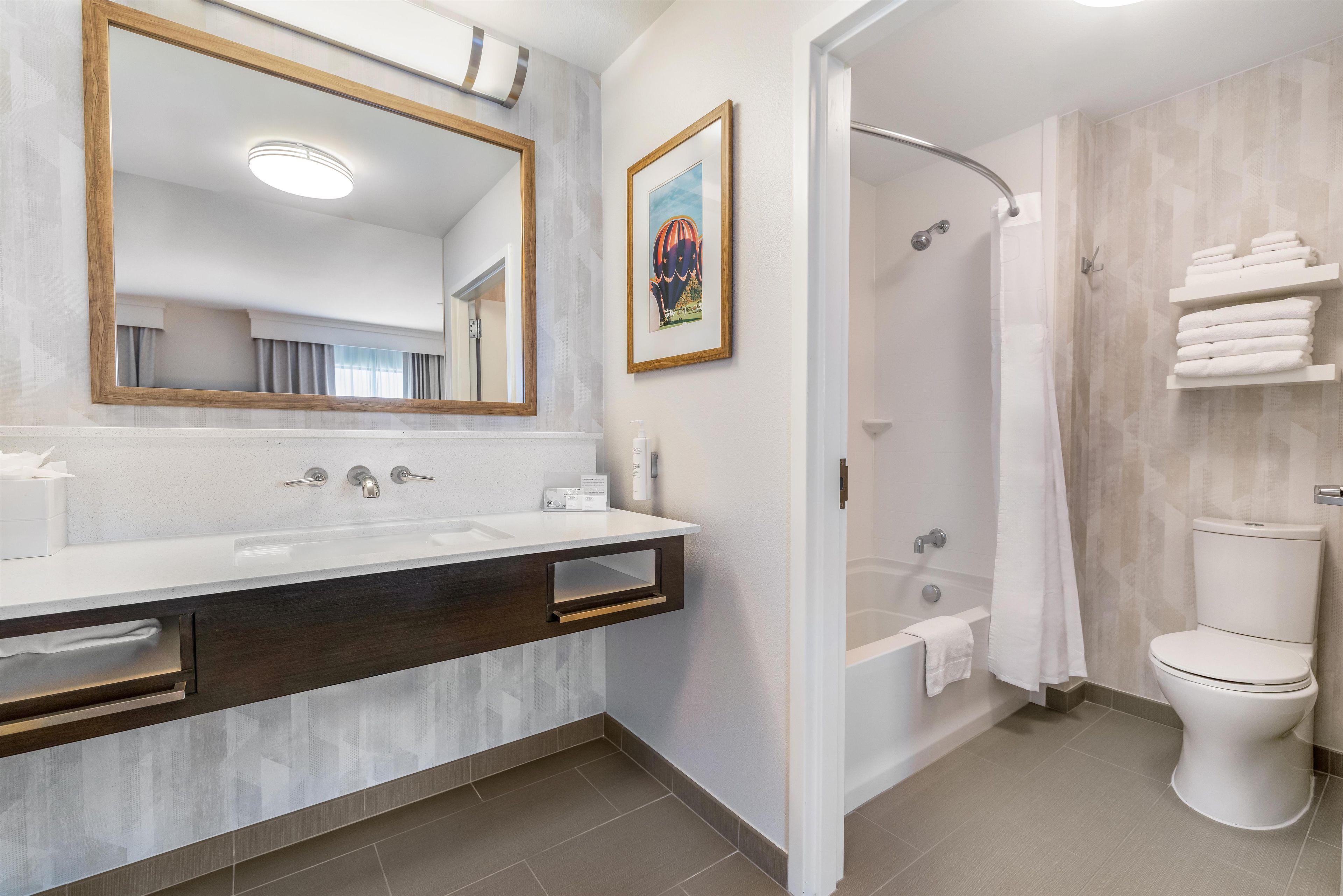 A modern bathroom with a large mirror, a shower, and a toilet.