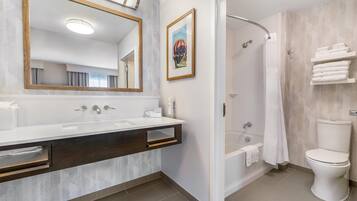 Un baño moderno con un espejo grande, ducha, inodoro y tocador con lavabo.