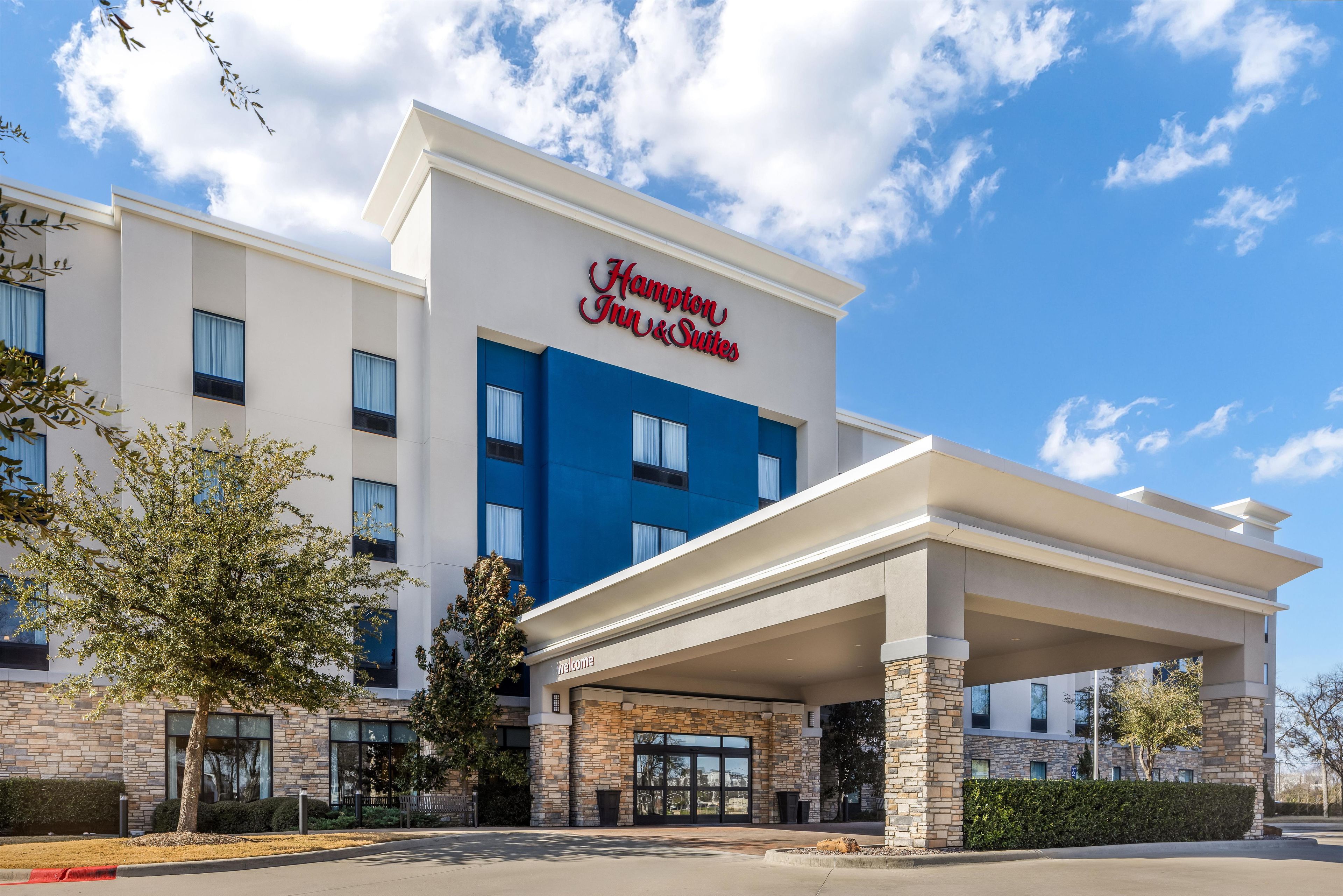 A Hampton Inn & Suites hotel with a modern facade, large windows, and a welcoming entrance.