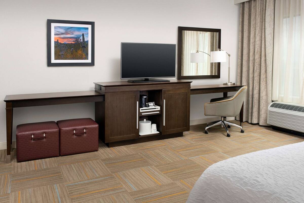Une chambre d’hôtel équipée d’un bureau, d’une télévision, d’un miroir, d’une chaise, d’un lit, d’un radiateur et de deux valises.