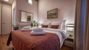 A hotel room with a large bed, a bedside table, a nightstand, a mirror, a painting on the wall, and a wooden wardrobe. - Boutique Residence by Little King (Prague)