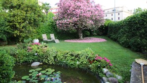 A garden with a pond, a pink flowering tree, and a bench. - Villa Ines (Venice)