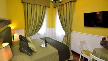 A hotel room with a bed, a TV, a table with a chair, and a window with curtains.