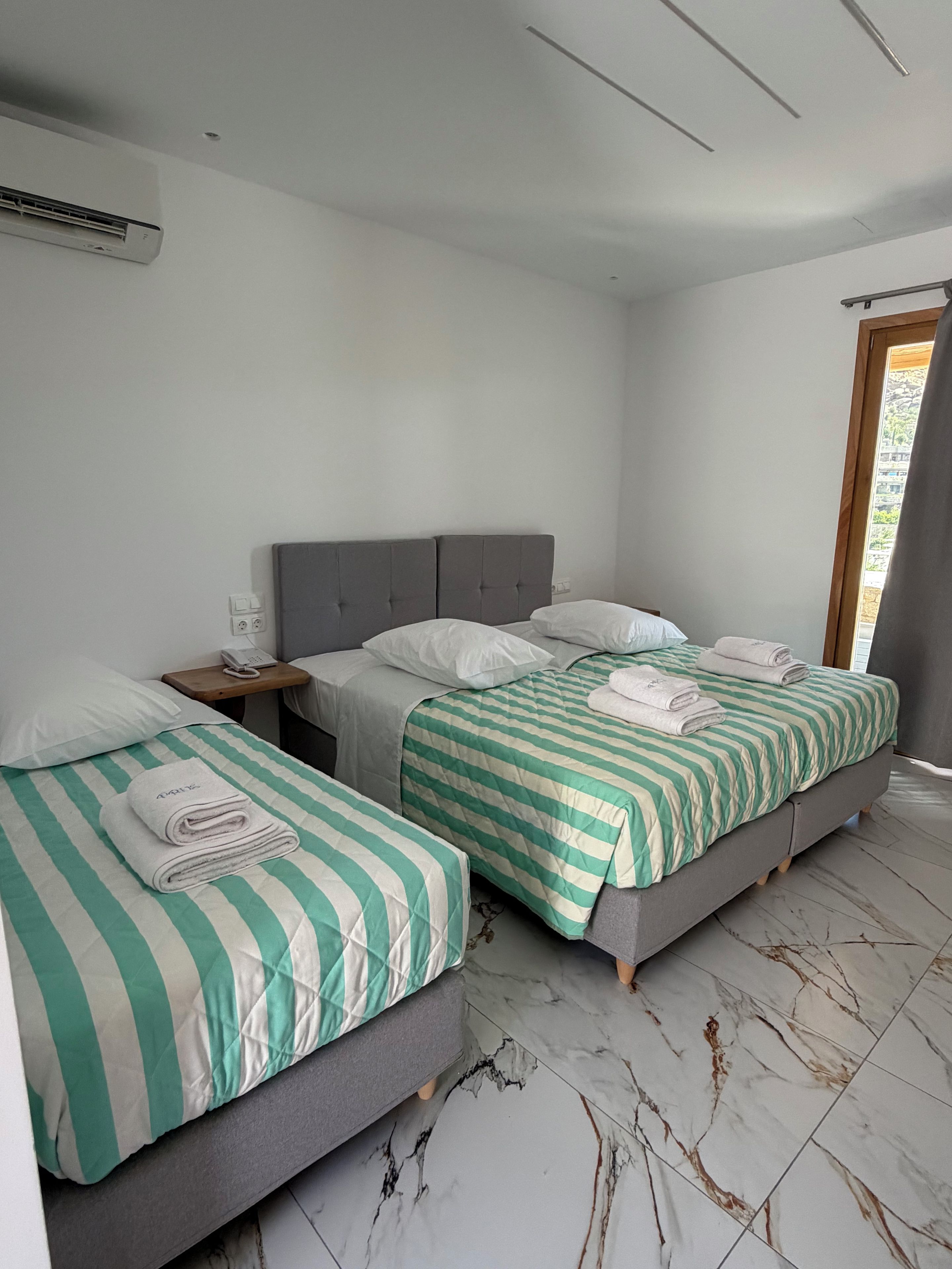 A hotel room with two beds, a bedside table with a phone, and a window with curtains.