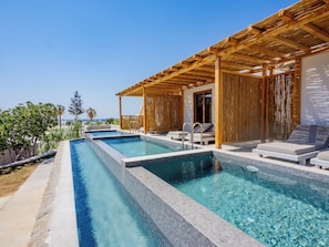 A pool area with multiple swimming pools, lounge chairs, and a wooden pergola. - Paradise Beach Resort (Mykonos)