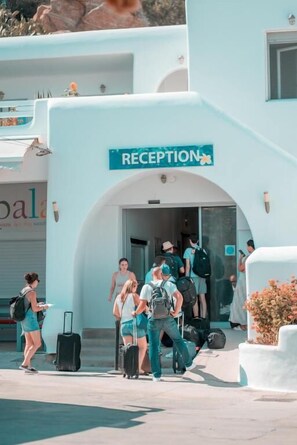 A reception area with a sign, people entering, and a building facade. - Paradise Beach Resort (Mykonos)
