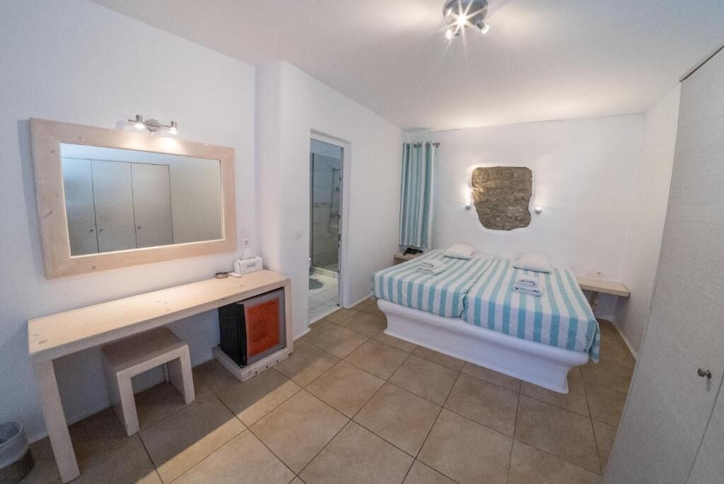 Quarto com cama, mesa de cabeceira, espelho e um banquinho.