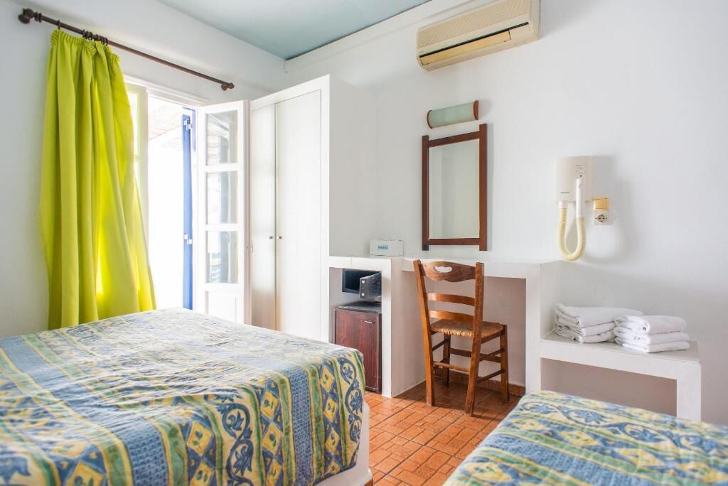 A hotel room with two beds, a desk, a chair, a mirror, a TV, and a bathroom with towels.