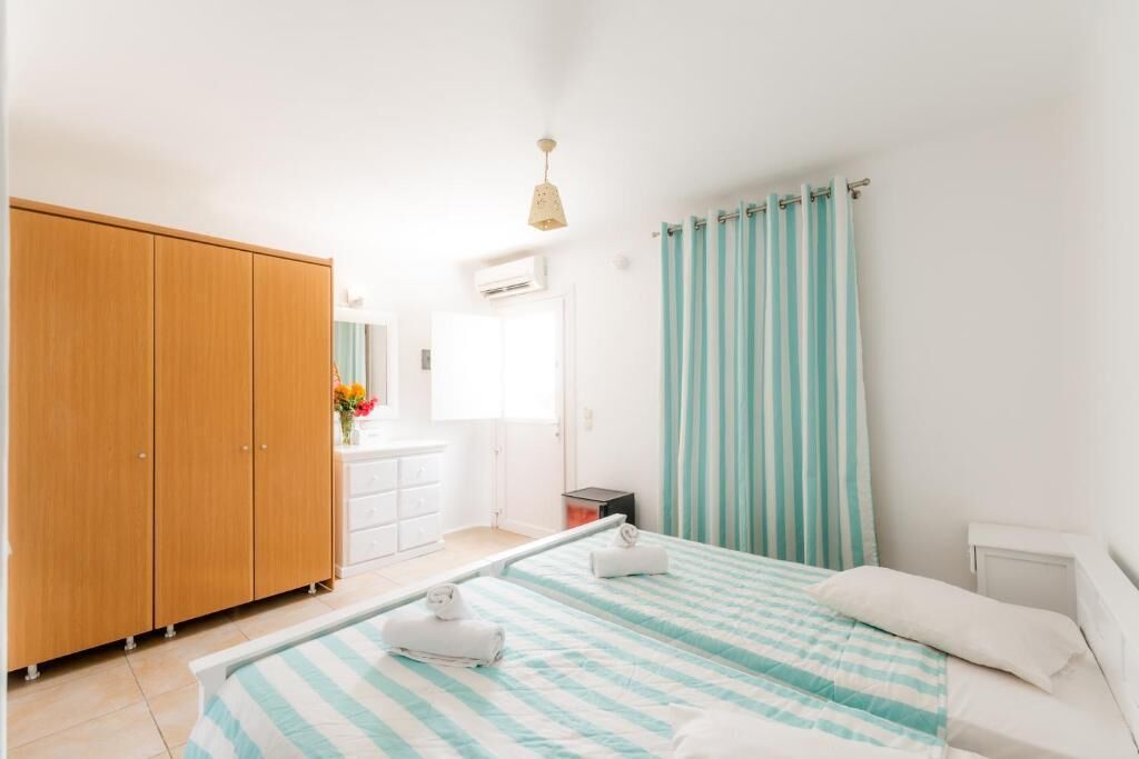 A bedroom with two beds, a wooden wardrobe, a white dresser, and a bathroom with a shower curtain.