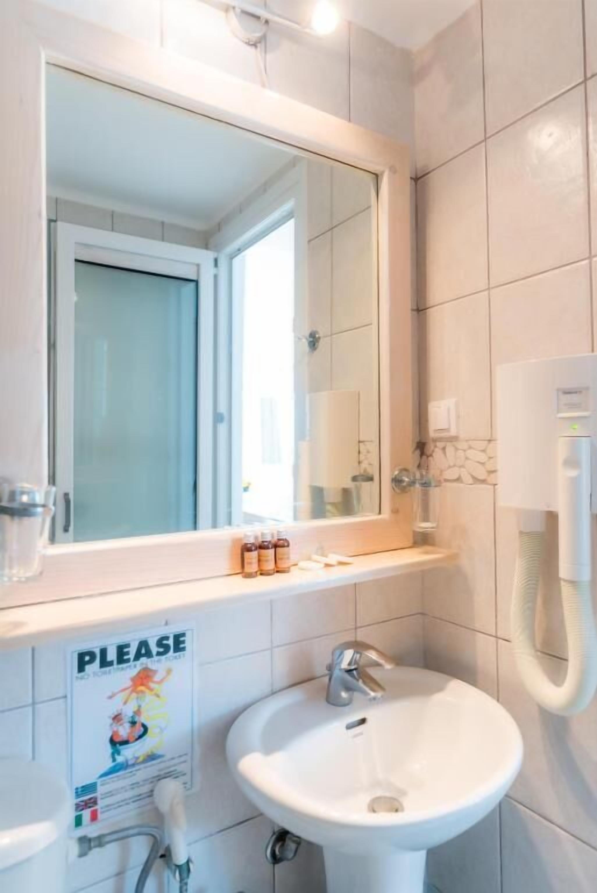 Une salle de bain avec un lavabo blanc, un miroir et un panneau indiquant « Veuillez » sur le mur.