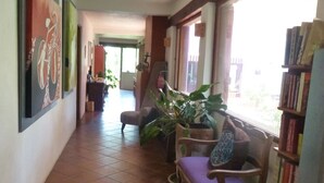 A hallway with a tiled floor, a chair with a cushion, a bookshelf, and a window with a view. - La Casa del Rio (Valle de Bravo)