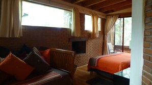 A cozy room with a brick fireplace, a wooden ceiling, and a bed with an orange bedspread. - La Casa del Rio (Valle de Bravo)