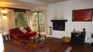 A cozy living room with a red sofa, a fireplace, a coffee machine, and a large window with curtains. - La Casa del Rio (Valle de Bravo)