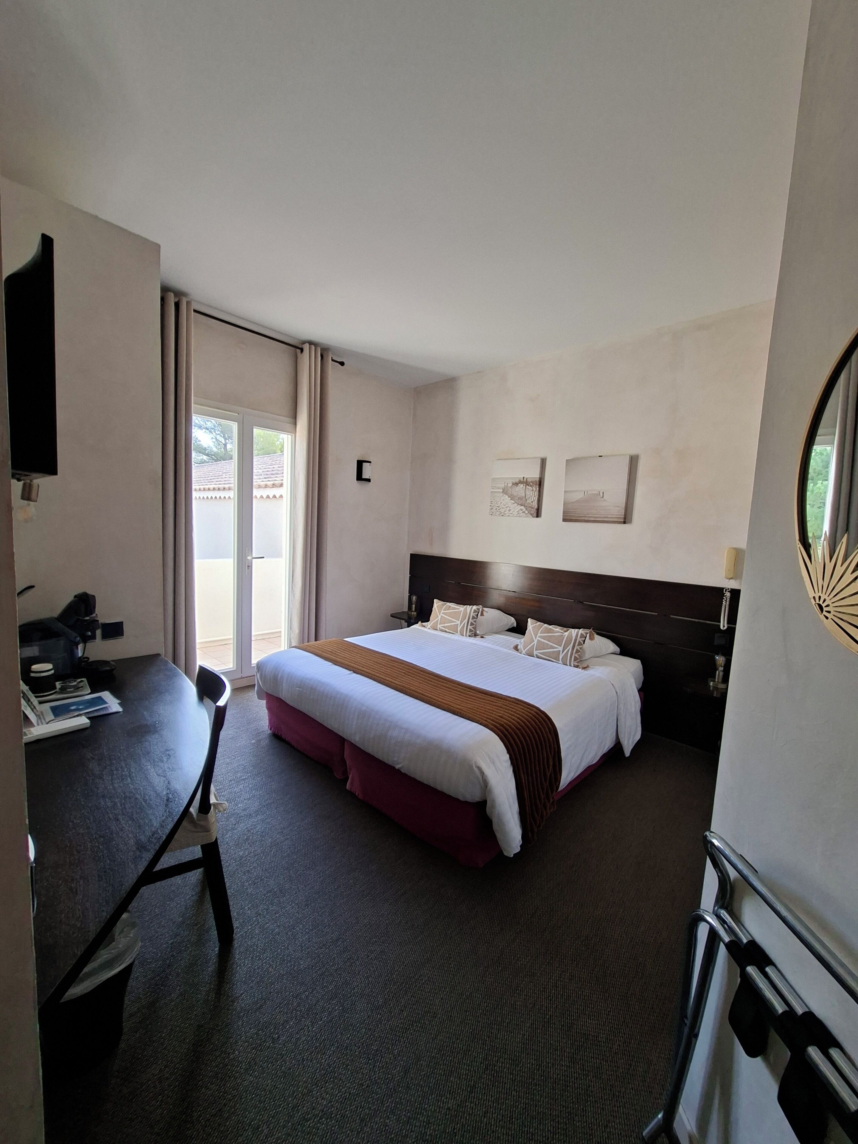 A hotel room with a large bed, a desk, a chair, a TV, and a sliding door to the outside.