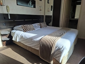 Una cama bien hecha con almohadones estampados, una mesita de noche con lámpara y un teléfono fijo en la pared.