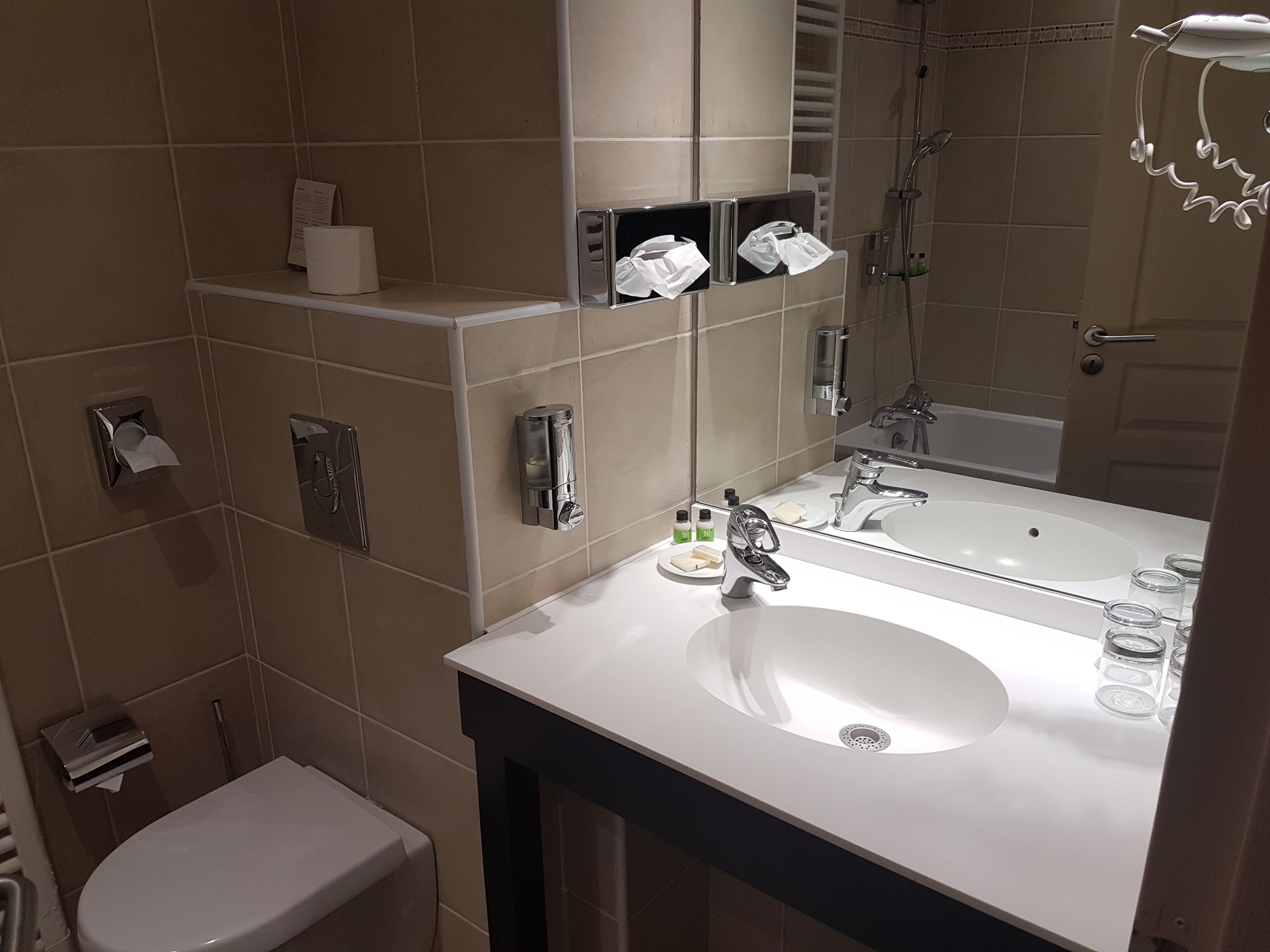 A modern bathroom with a white sink, mirror, and shower. There are toiletries on the sink and a towel rack above the mirror.