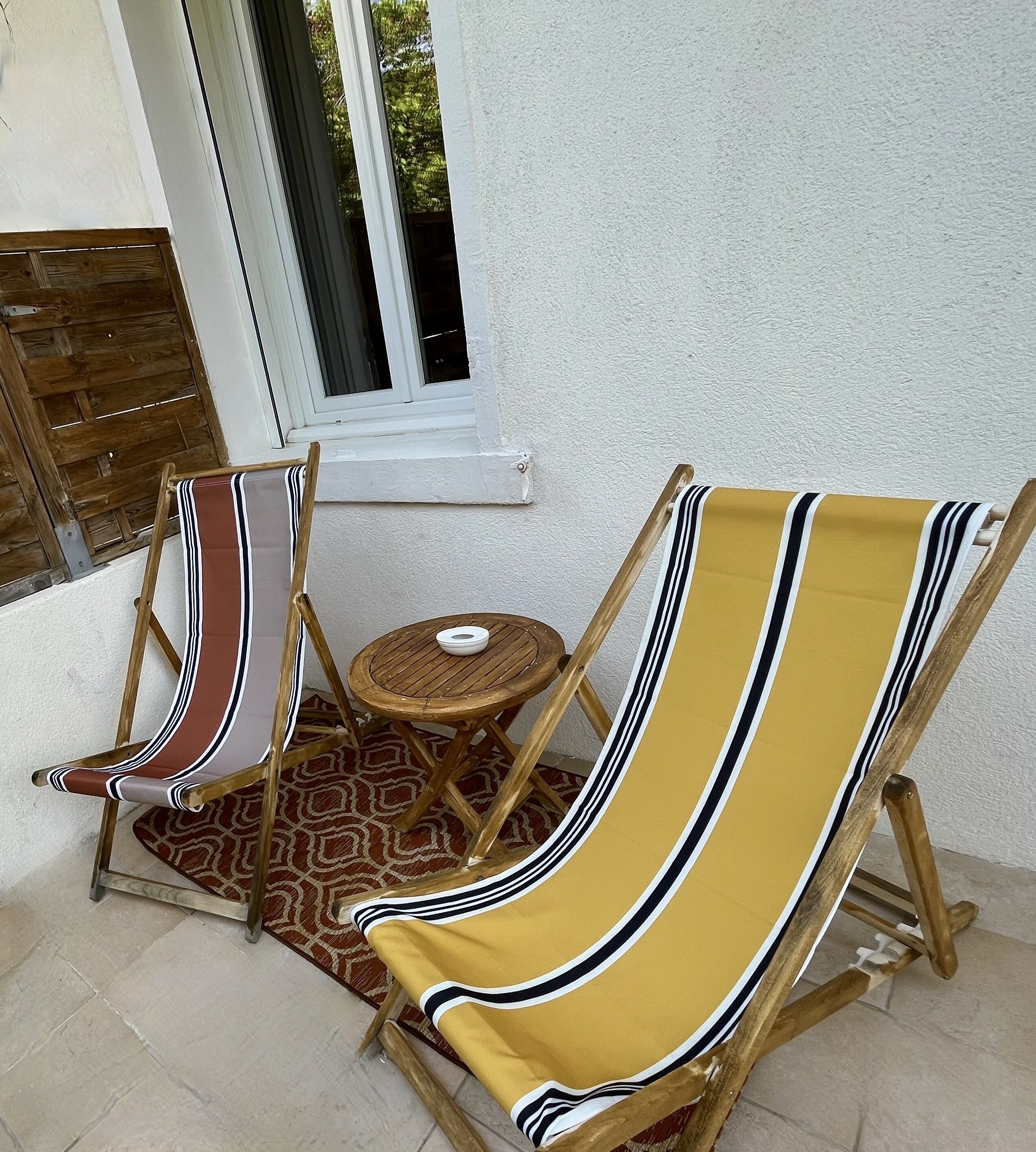 Two wooden lounge chairs with striped cushions, a small round wooden table, and a patterned rug on a tiled floor.