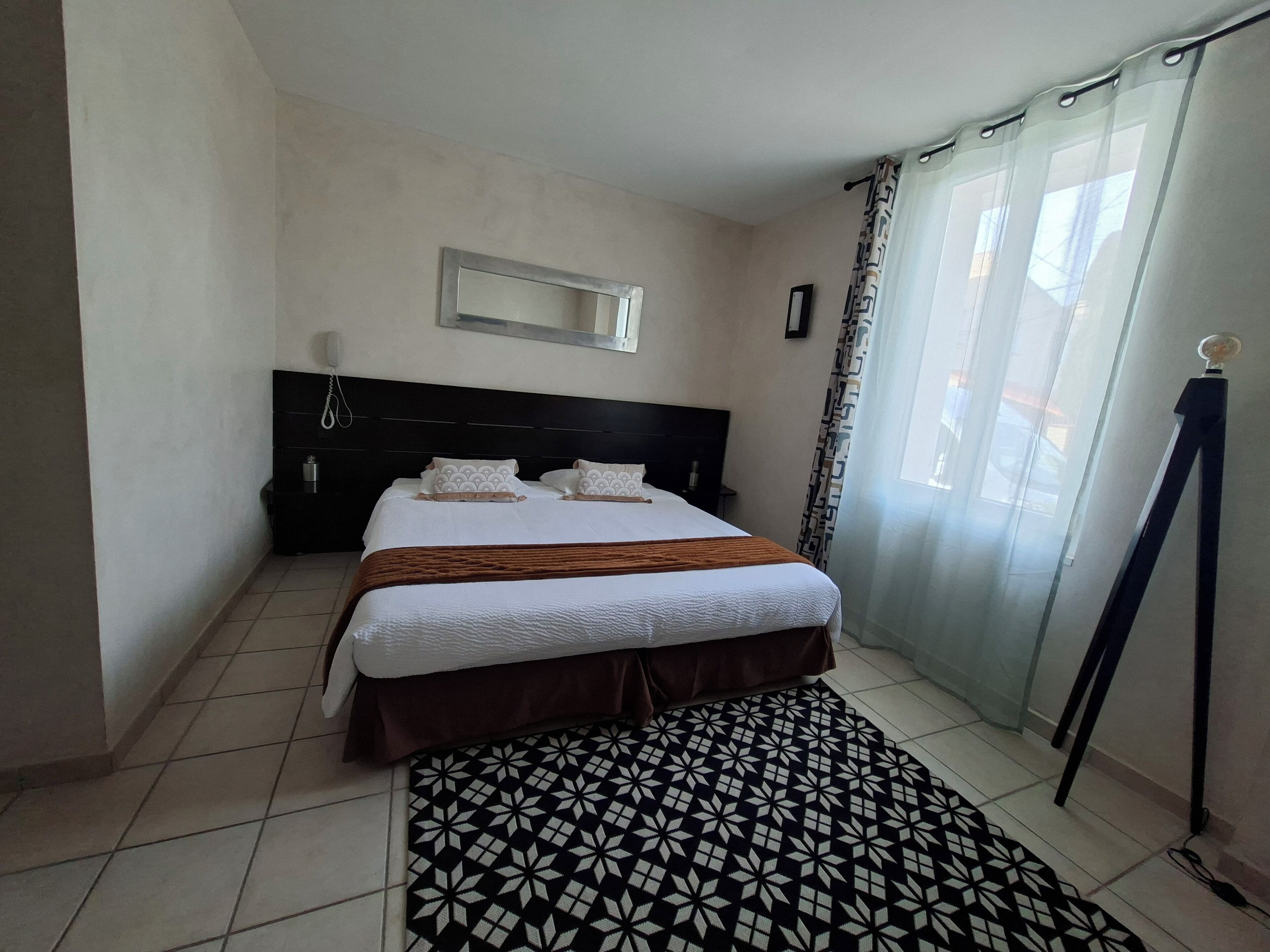 Una habitación de hotel con una cama, una mesita de noche, un espejo y una alfombra estampada.