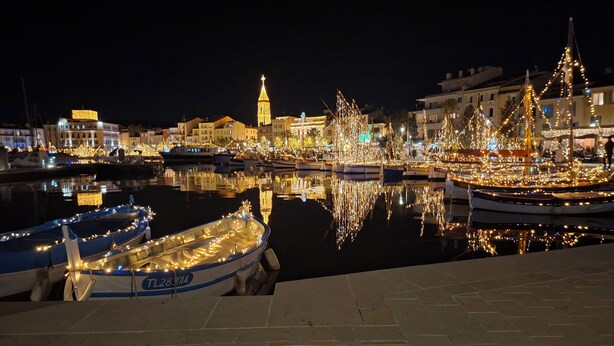 A marina at night with boats docked and illuminated by string lights, a prominent tower in the background, and a calm water surface reflecting the lights. - Hôtel Synaya (Sanary-sur-Mer)
