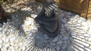 A stone Buddha statue in a garden setting with a wooden fence and pebbles. - Hôtel Synaya (Sanary-sur-Mer)